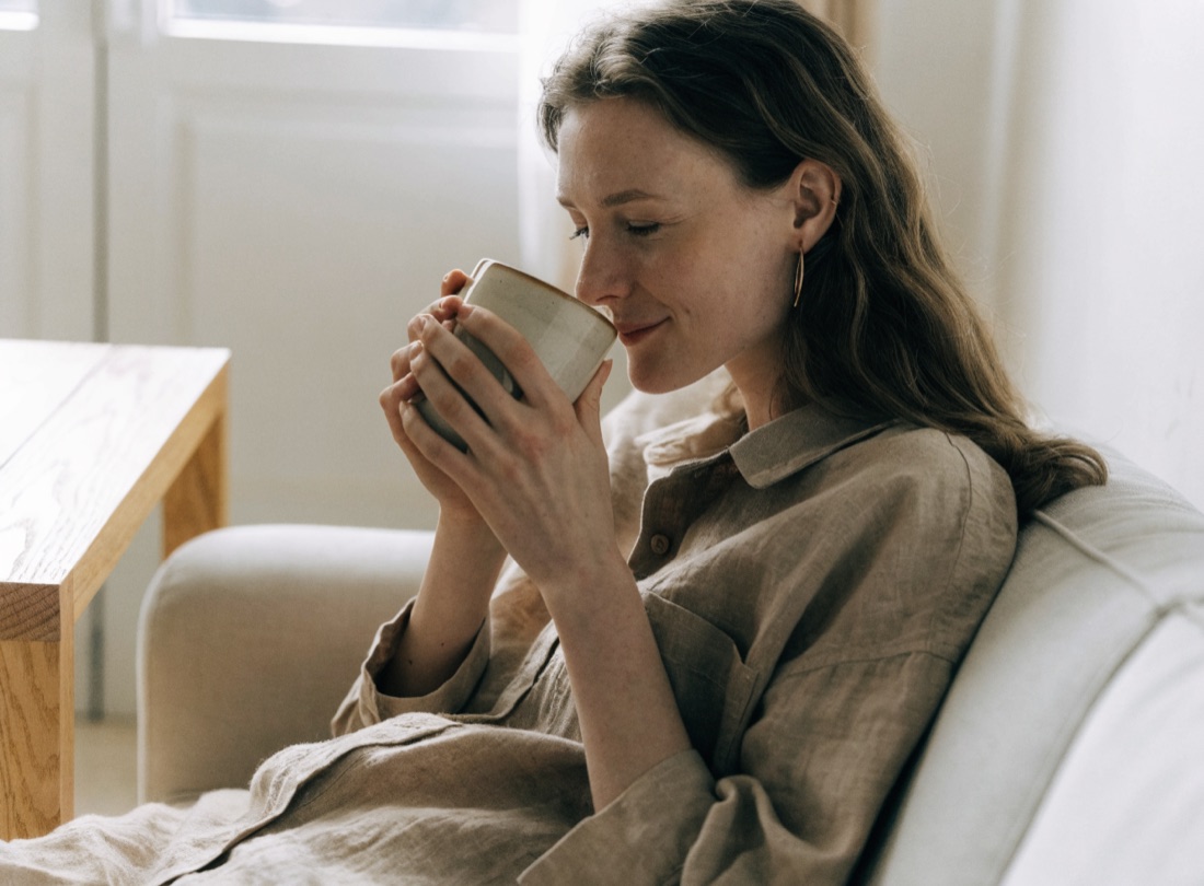 Femme détendue sur un canapé, une tasse chaude entre les mains