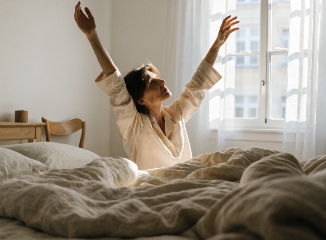 Femme qui s'étire au réveil devant une fenêtre baignée de lumière